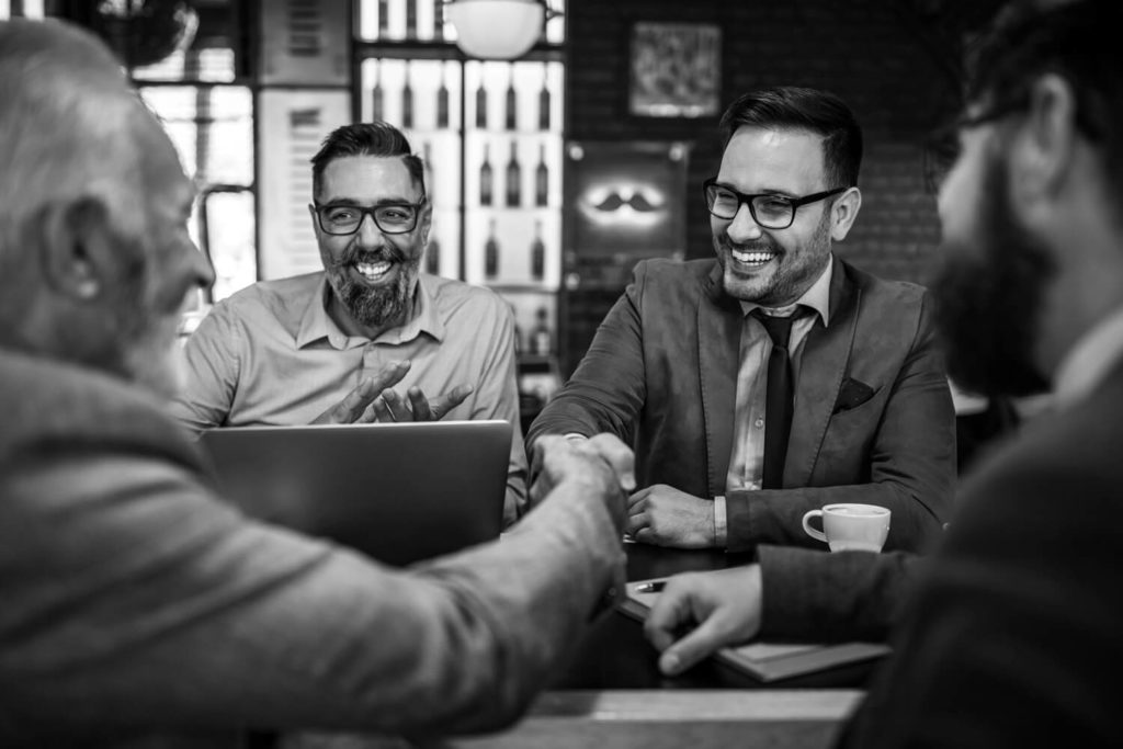 Four men of various ages and ethnicities in a meeting smiling